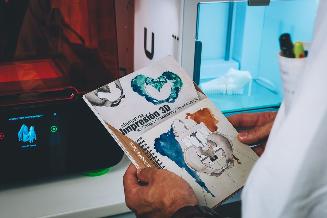 Ejemplar del Manual de Impresión 3D en Cirugía Ortopédica y Traumatología junto a una impresora 3D